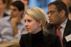 Photo of Elizabeth Holmes listening to a speaker in a crowd.
