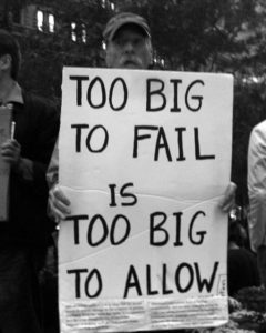 Black and white image of man holding a sign that says, "Too big to fail is too big to allow" in all capital letters.