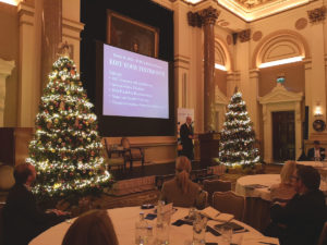 Picture of Richard M. Bowen speaking at IoB conference with Christmas trees on both sides of the projected slides.