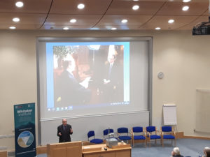 Photo of Richard M Bowen speaking at The Whitaker Institute with a slide from his 60 Minutes interview.