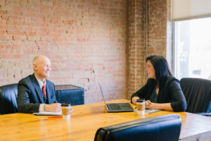 Man and woman in suits meeting at large wooden table.