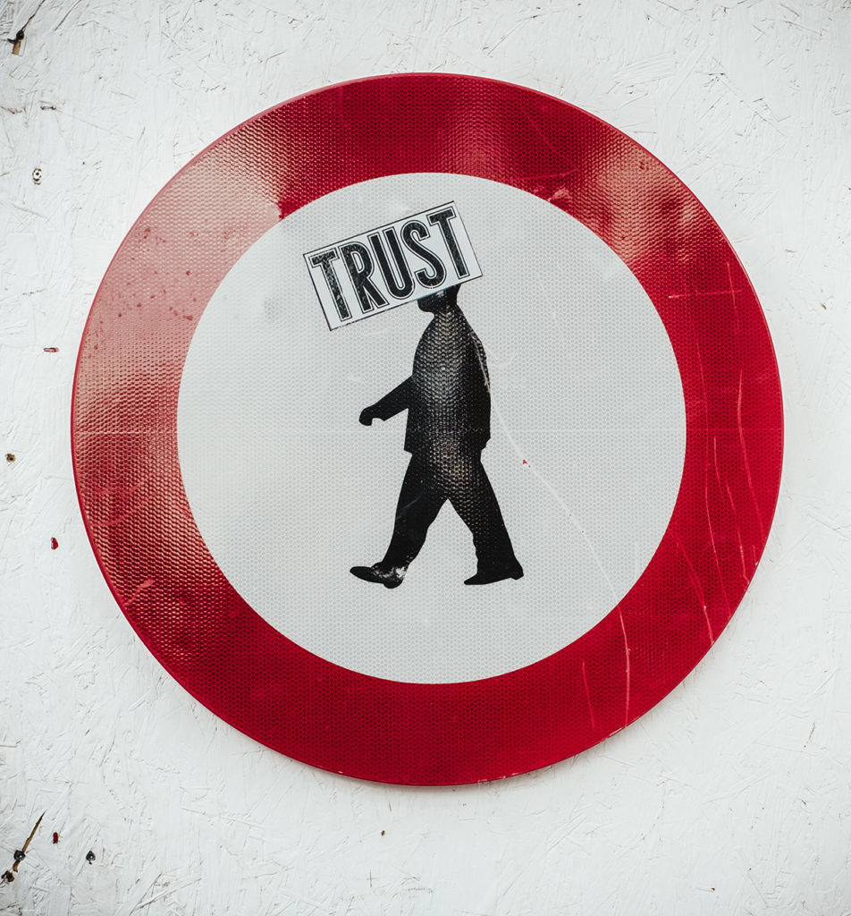 Image of a man walking to the left inside a circle, the word TRUST in a box across his head.