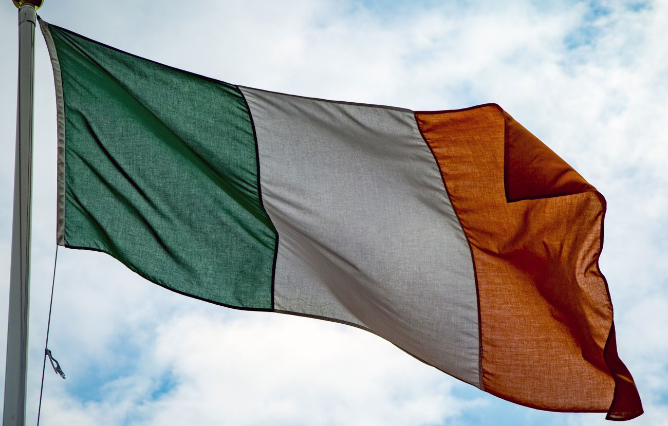 Irish flag against a blue sky with white clouds.